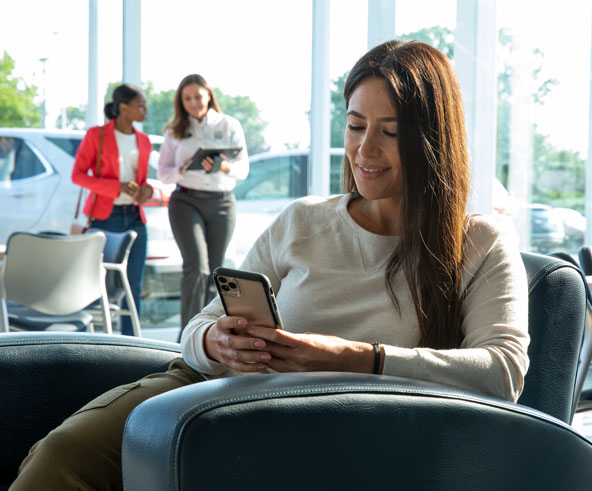 Woman sitting at a car dealership looking at a cellphone